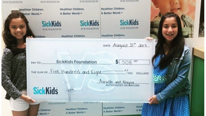 Aarushi and Nayza holding a check for $508.00 made out to SickKids Foundation.